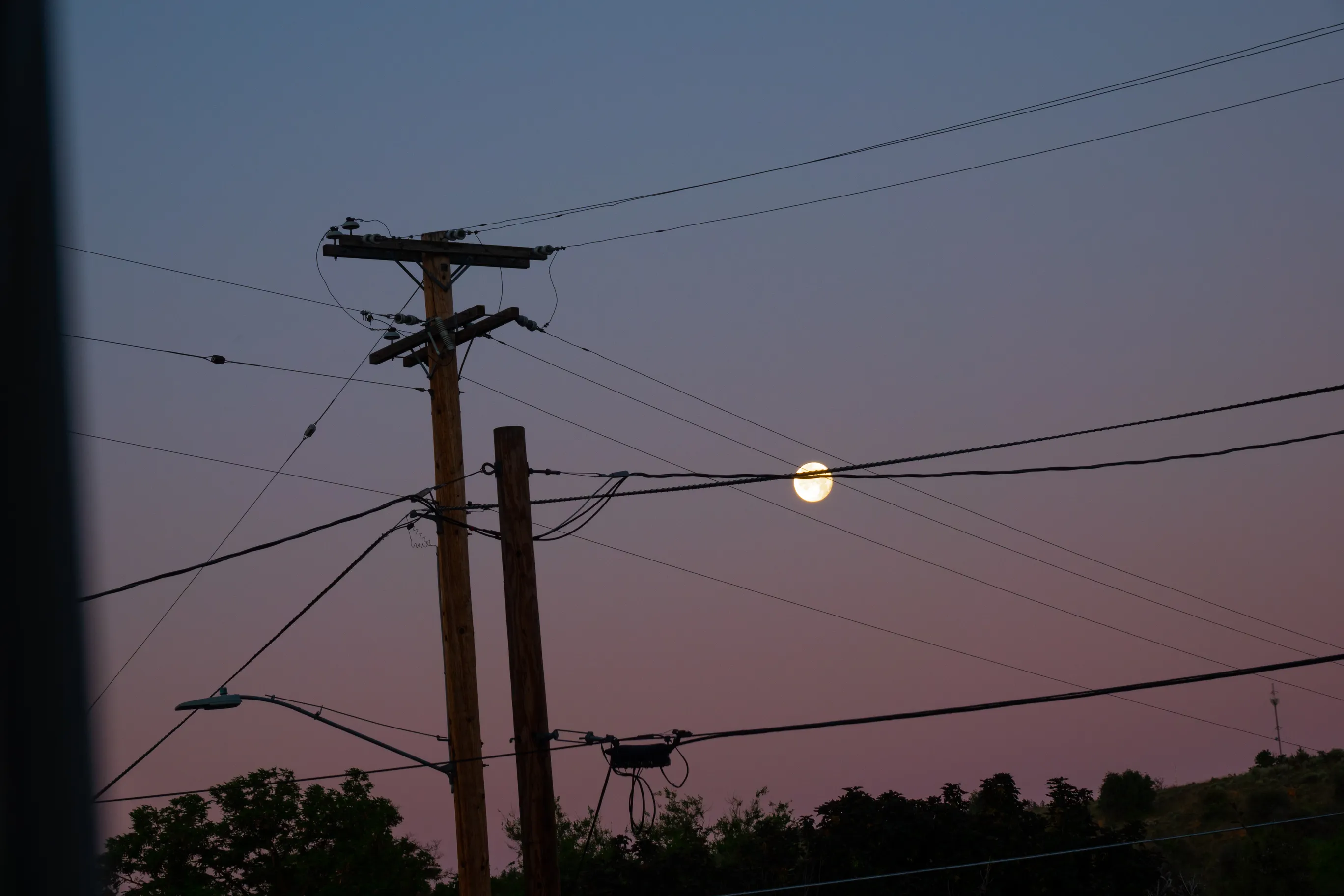 A photo of the full moon crossing power lines during the early sunrise