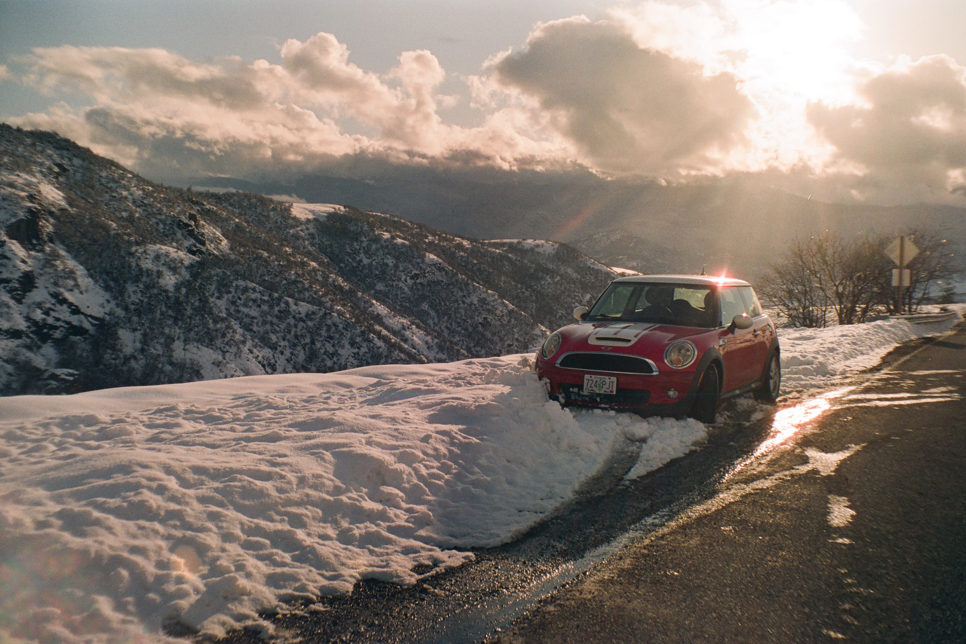 A photo of a red mini cooper on a snowy mountain road
