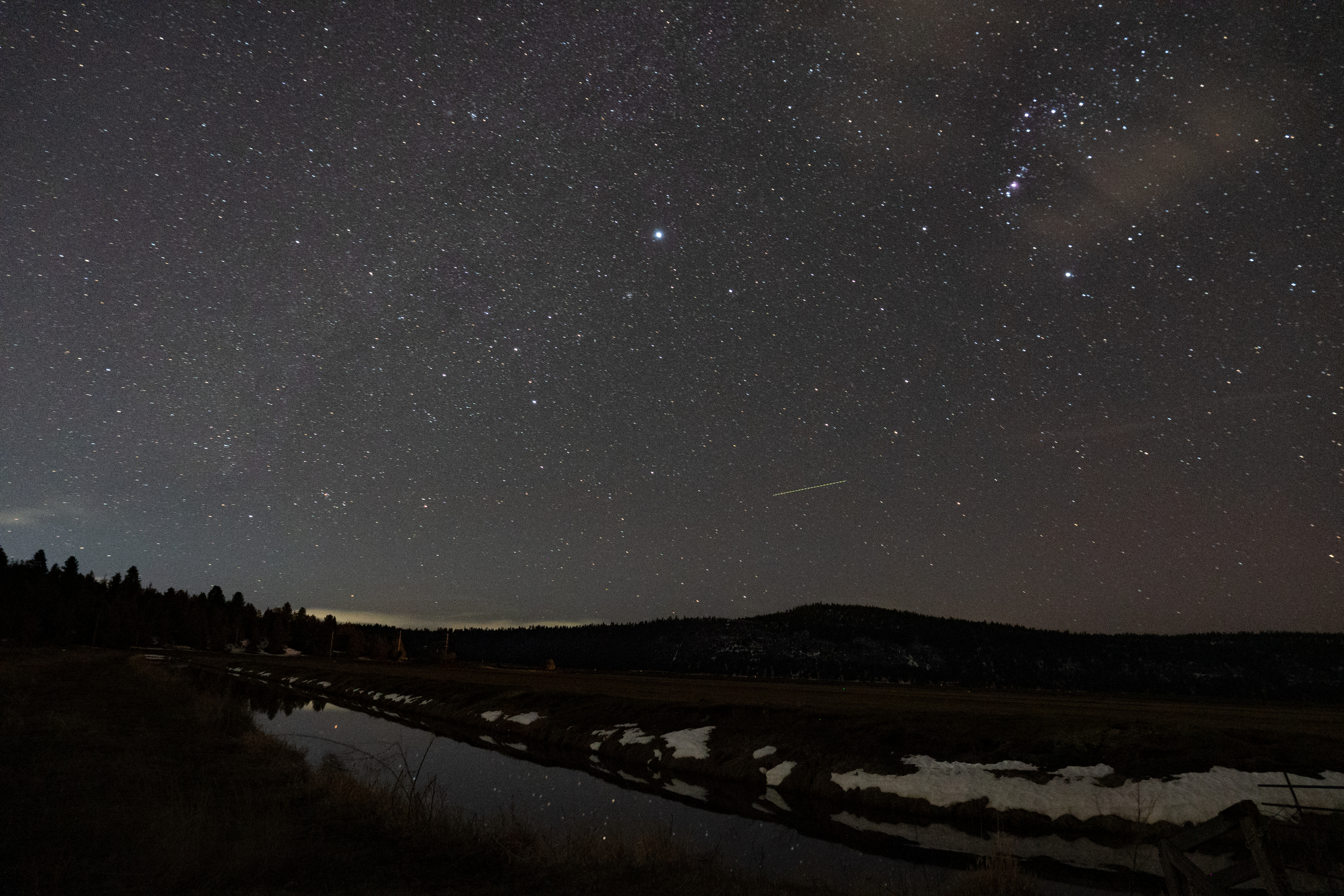 A photo of the night sky with some mountains and fields in the foreground
