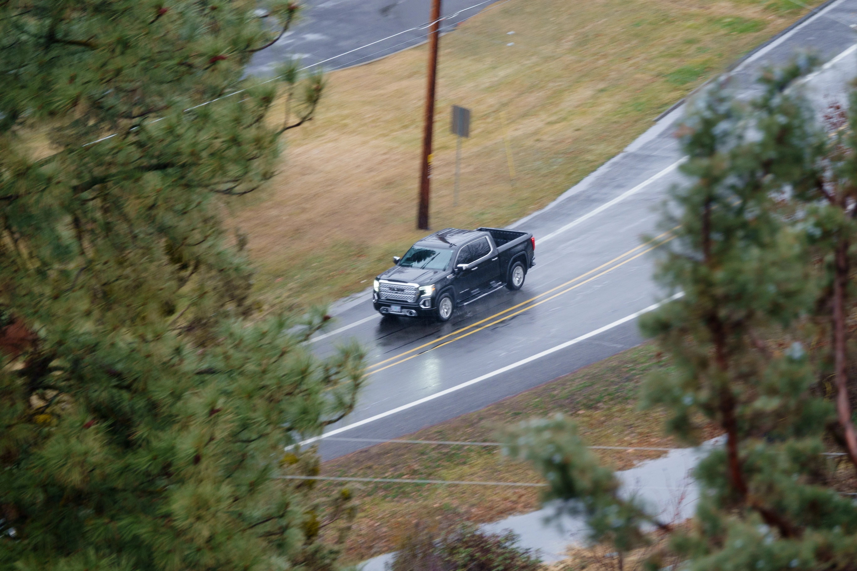 A photo of a black truck driving down a rainy road